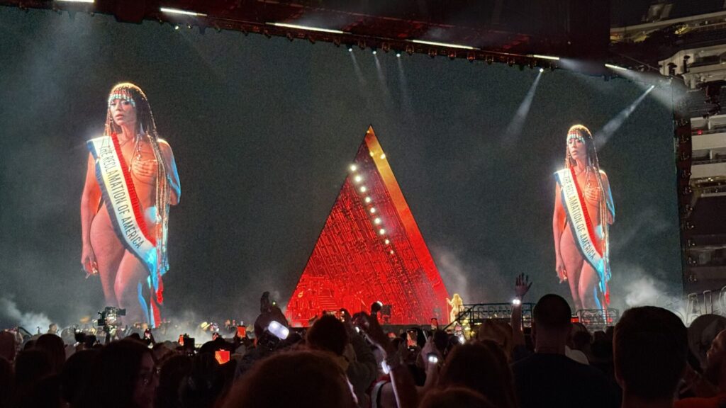 The stage screen of the Cowboy Carter Tour showing a photo of Beyonce in the nude wearing a sash that reads "The Reclamation of America".